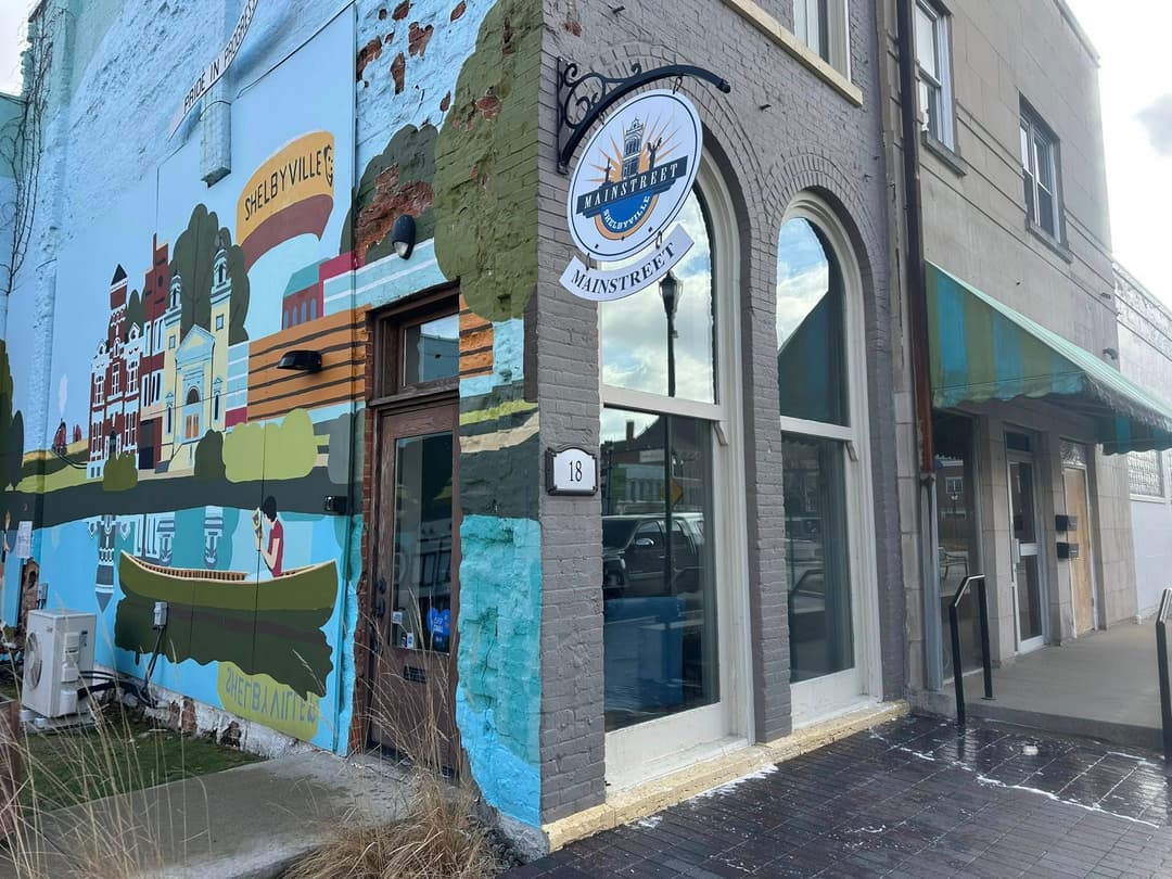Mural on building showcasing small-town scenery alongside a storefront with an awning.