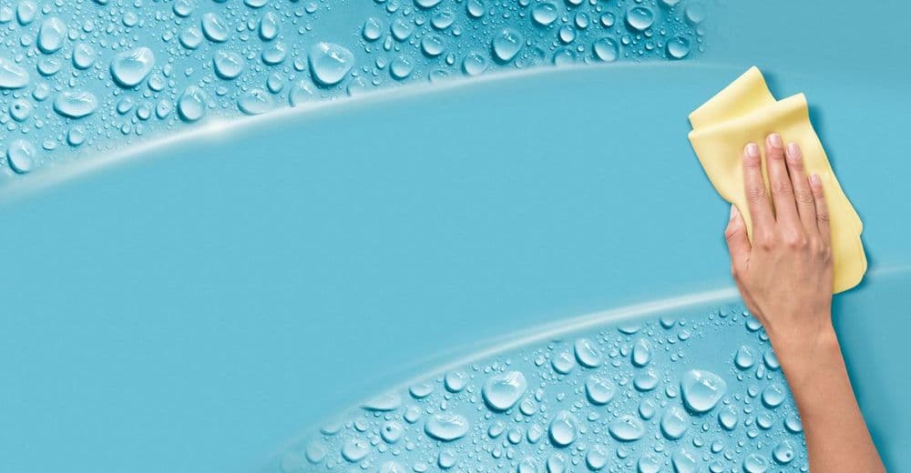 Person cleaning a smooth blue surface with a yellow cloth, surrounded by water droplets.